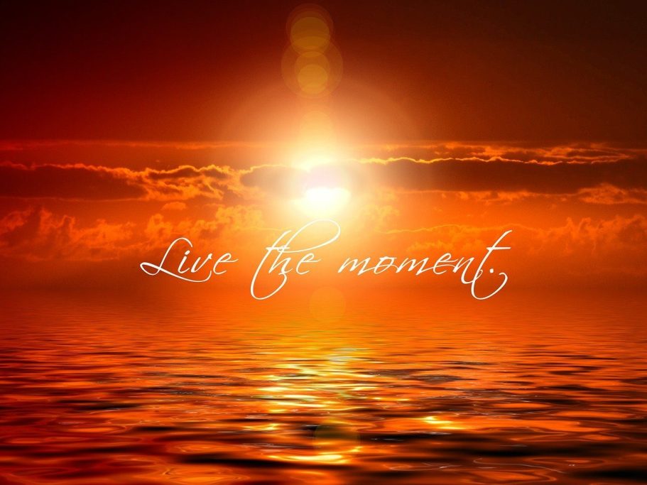 photo of an orange sunset with the sea at the bottom and clouds in the sky. White writing across saying Live the Moment