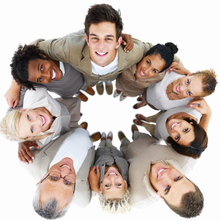 photo of nine adults (men and women) linking arms in a circle taken from above their heads as they gaze up at the camera with smiles.